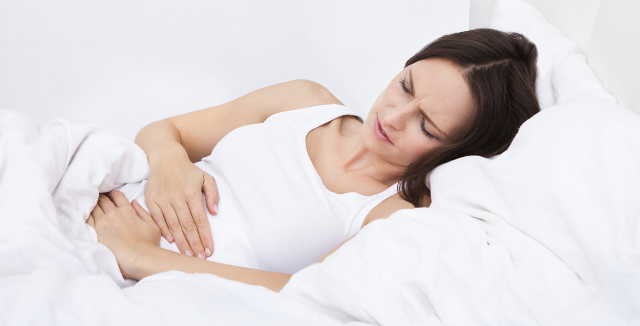 Kvinna ligger i sängen med smärtor på grund av ibs-mage.